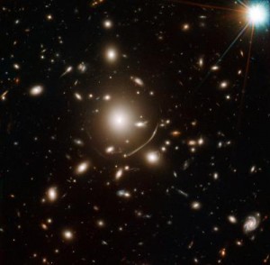Il gigantesco ammasso di galassie ellittiche nel centro di questa immagine contiene tanta massa di materia oscura che la sua gravità curve di luce. Questo ha permesso la scoperta della galassia più antica mai osservata. Crediti: NASA, ESA, J. Richard (CRAL) and J.-P. Kneib (LAM). Acknowledgement: Marc Postman (STScI)
